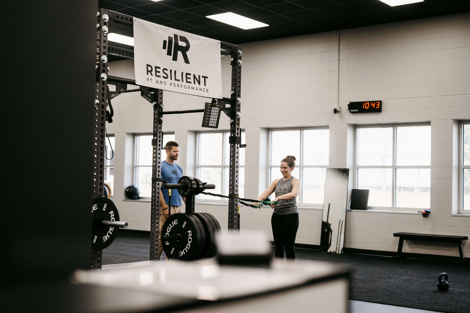 Personal trainer guiding a woman through a resistance-band exercise in a strength-training gym.