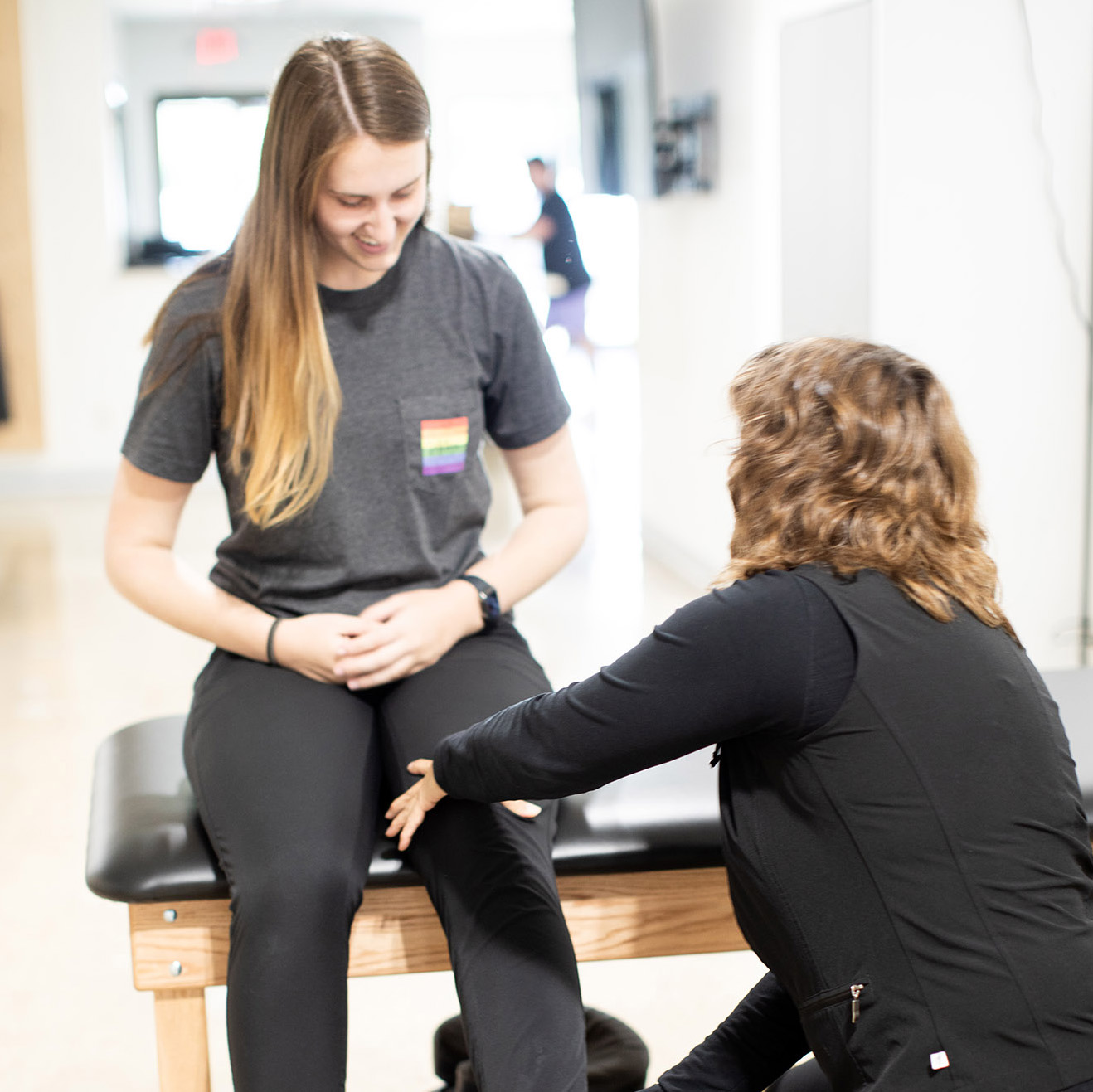 Physical therapist examining a seated patient’s knee and lower leg.