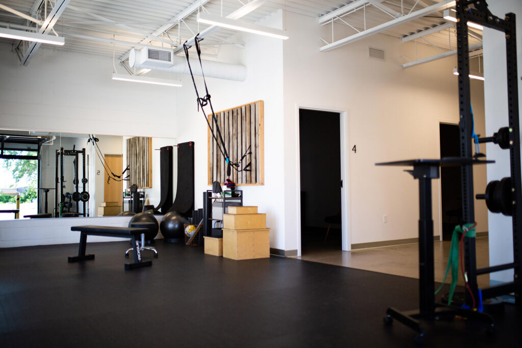 Modern rehabilitation gym with suspension trainers, exercise balls, plyometric boxes, and strength equipment.